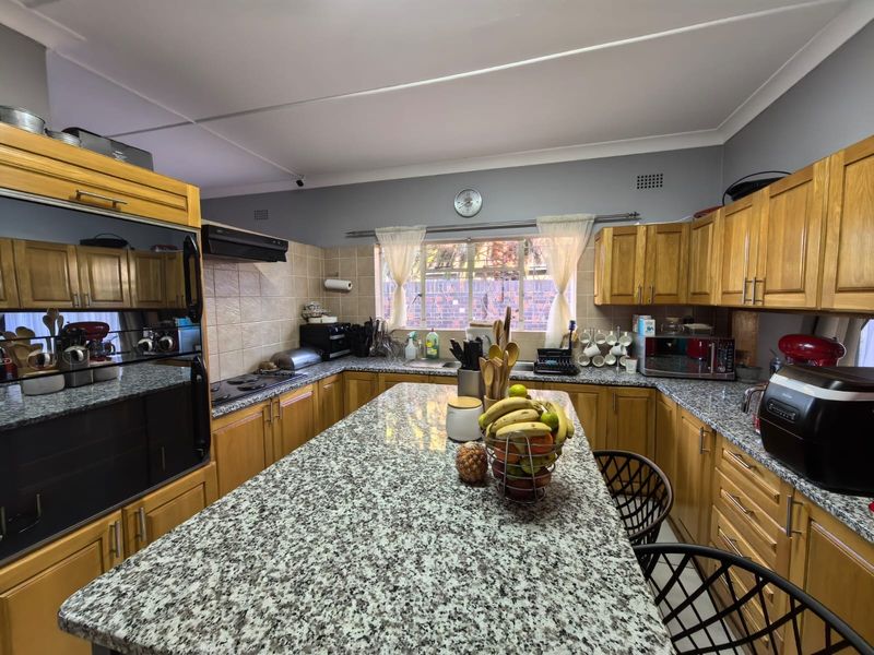 A functional kitchen featuring granite countertops, wooden cabinetry, a central island, and built-in cooking appliances, offering a practical layout for meal preparation.