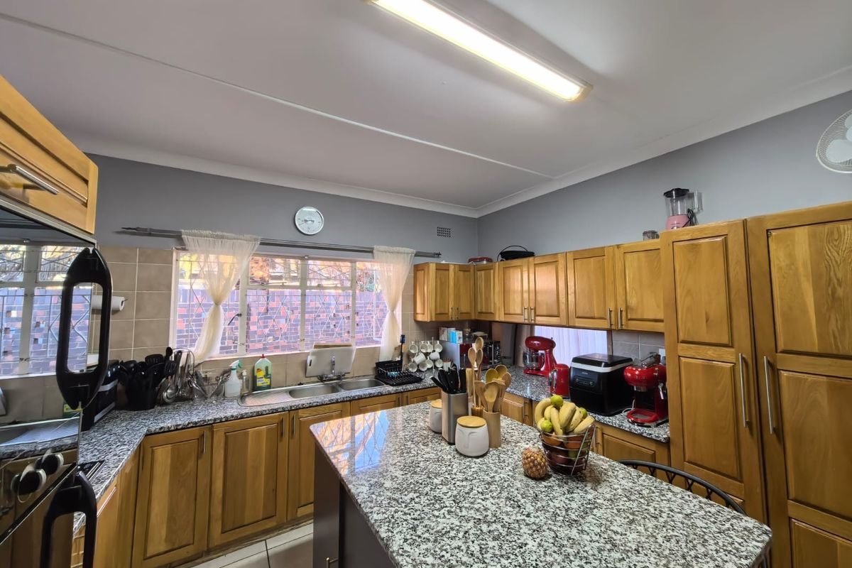 A functional kitchen featuring wooden cabinetry, granite countertops, a central island, and a double basin sink with tiled backsplash.