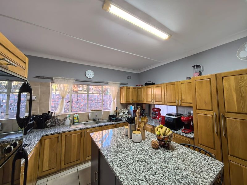 A functional kitchen featuring wooden cabinetry, granite countertops, a central island, and a double basin sink with tiled backsplash.