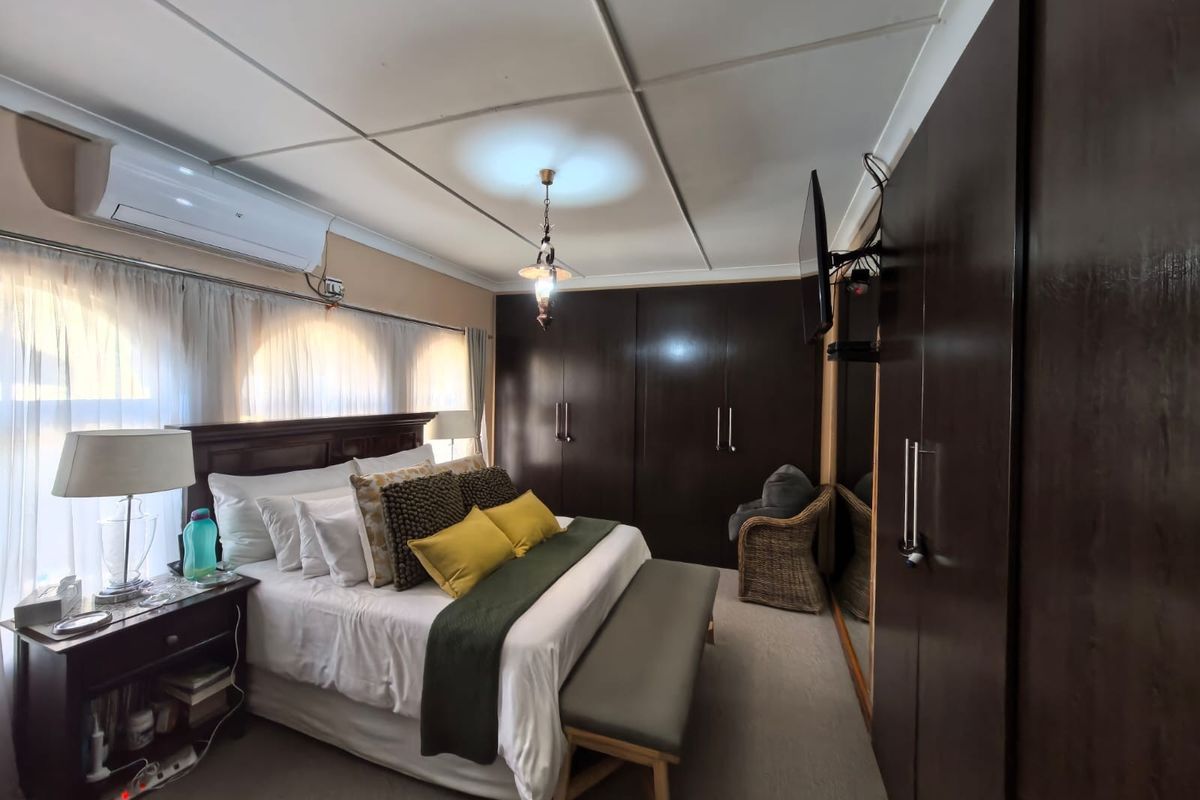 A well-maintained bedroom featuring extensive dark wood built-in cupboards, a split-system air conditioner, and neutral carpeting.