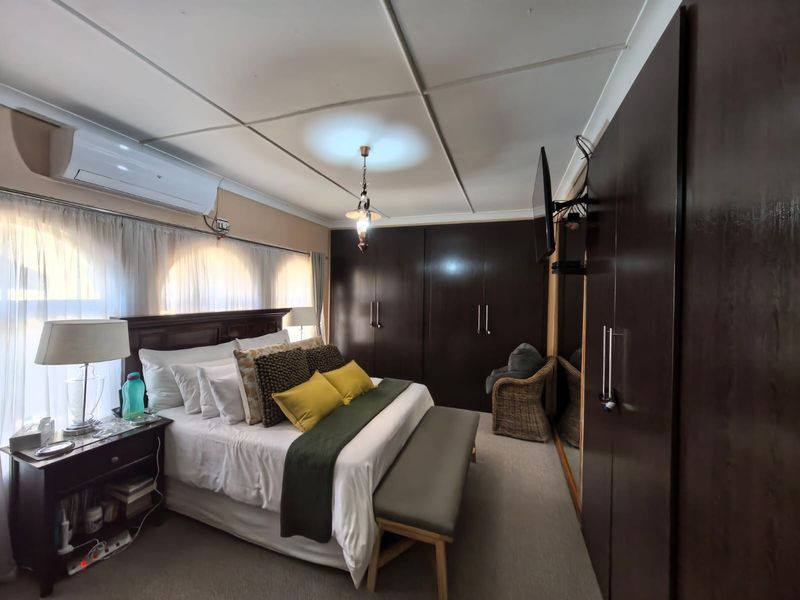 A well-maintained bedroom featuring extensive dark wood built-in cupboards, a split-system air conditioner, and neutral carpeting.