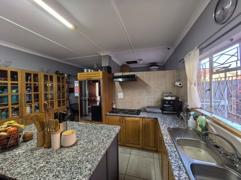 A functional kitchen featuring wooden cabinetry, granite countertops, a built-in oven, hob, extractor fan, and a double basin sink with tiled backsplash.
