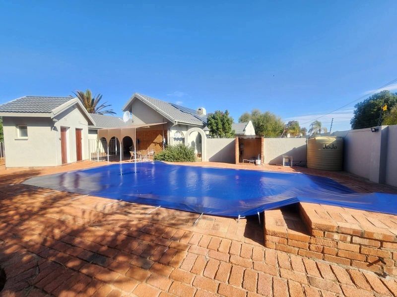 Outdoor pool area featuring brick paving, a covered patio, built-in braai, and a water storage tank.