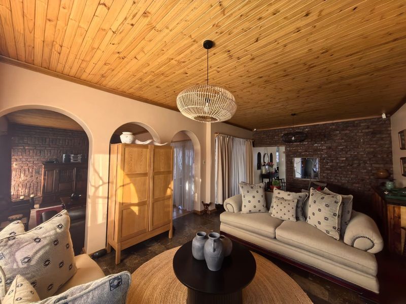 Spacious living room featuring a warm timber ceiling, exposed brick wall, and elegant arched doorways leading to adjacent living areas.
