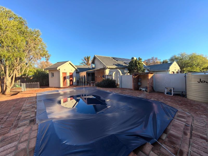 Rear garden area featuring a swimming pool with a cover, brick paved surround, solar panels on the roof, and a water storage tank.