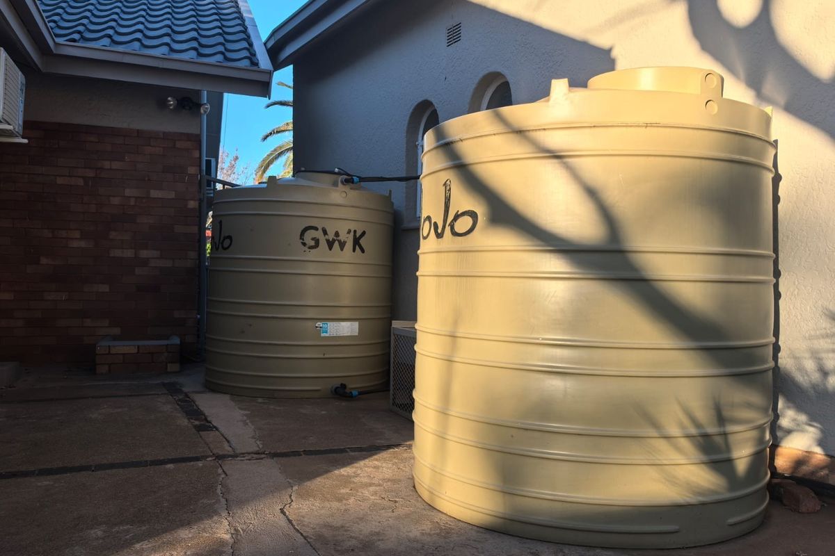 Rear exterior area featuring two large water storage tanks positioned on concrete paving adjacent to the house structure.