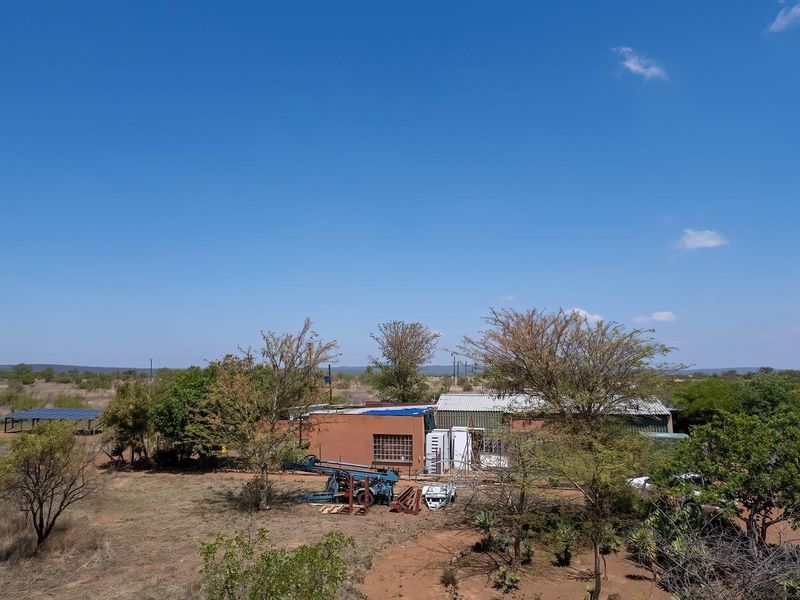Aerial view of a farm property featuring a main structure with a metal roof, solar panel installation, and surrounding rural landscape.