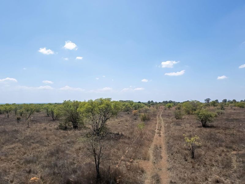 An expansive aerial view of the farm landscape featuring natural vegetation, open fields, and a dirt access track.