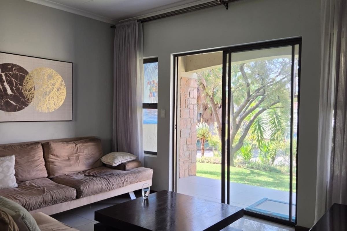 A bright living room featuring tiled floors, recessed lighting, and large sliding glass doors that provide direct access to the outdoor patio and garden.