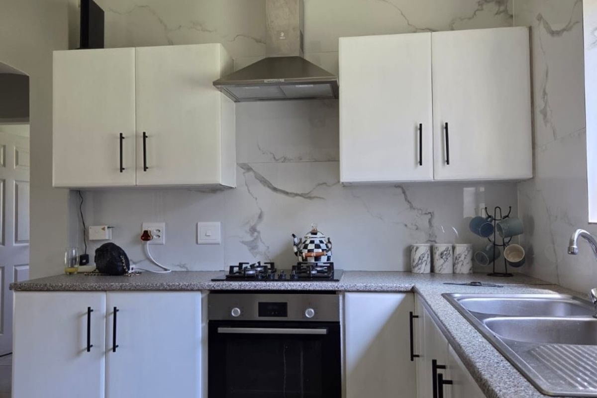A modern kitchen featuring white cabinetry, marble-effect splashbacks, stone-look countertops, and integrated stainless steel appliances including an oven and gas hob.