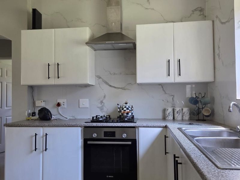 A modern kitchen featuring white cabinetry, marble-effect splashbacks, stone-look countertops, and integrated stainless steel appliances including an oven and gas hob.