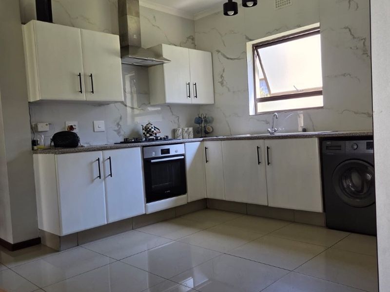 Modern kitchen featuring white cabinetry, marble-look splashbacks, granite countertops, built-in oven, extractor fan, and polished porcelain floor tiles.