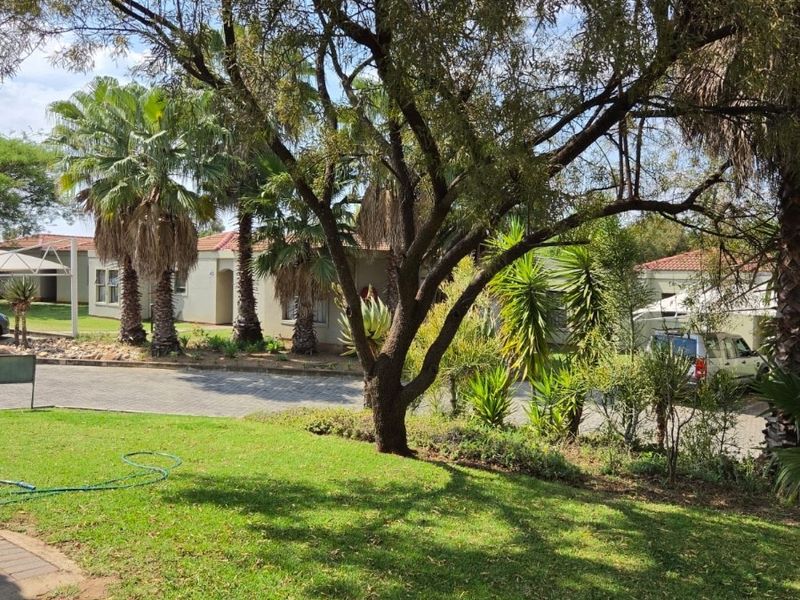 A well-maintained garden area featuring mature trees, lush lawn, and a paved driveway leading to the residential units.