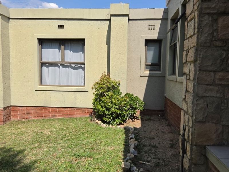 A view of the rear exterior featuring plastered walls, stone cladding accents, and a small garden area with a brick plinth foundation.