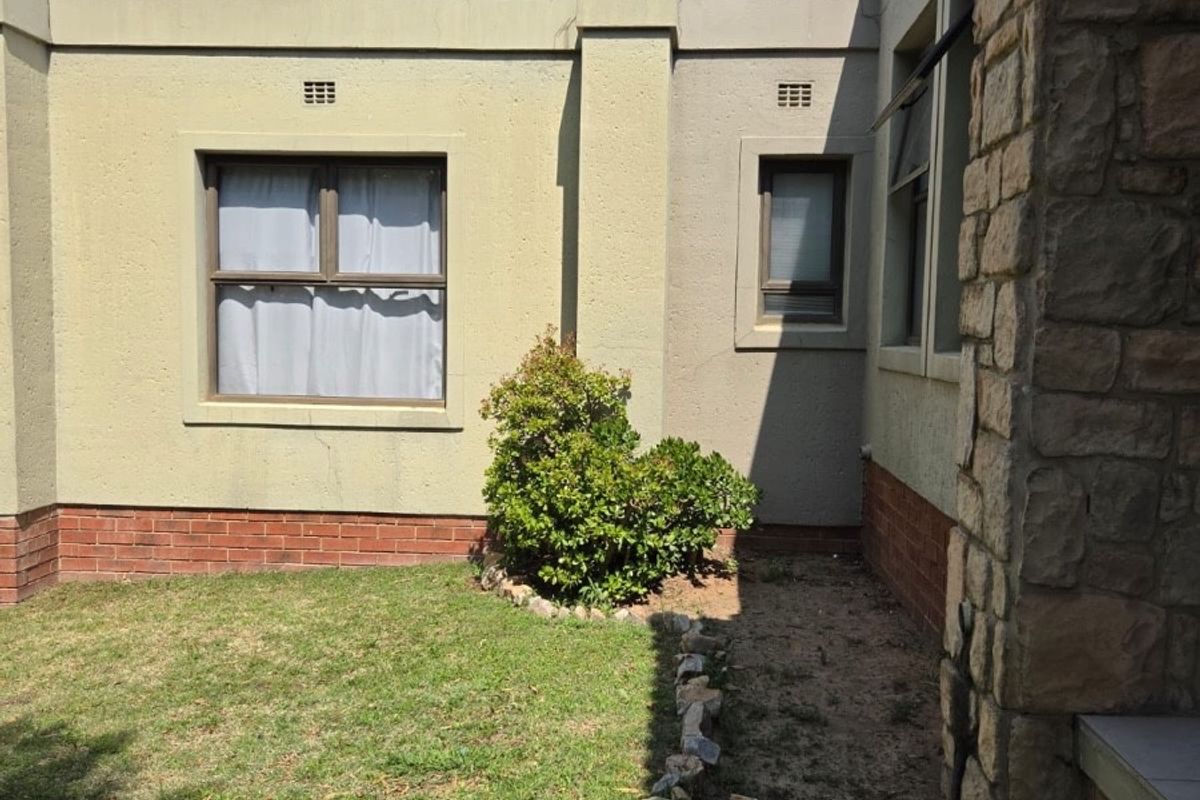 A view of the rear exterior featuring plastered walls, stone cladding accents, and a small garden area with a brick plinth foundation.