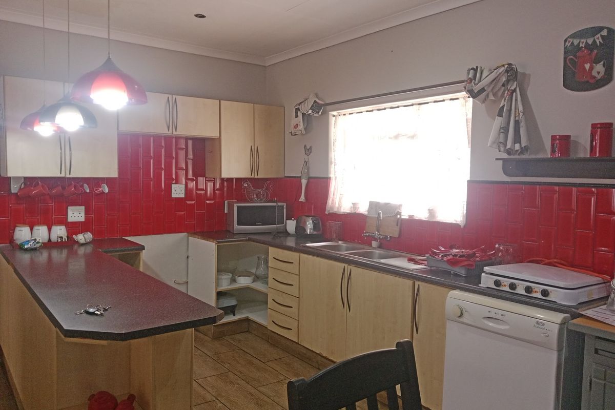 A functional kitchen featuring laminate cabinetry, a vibrant red subway tile backsplash, double bowl sink, and a breakfast bar with tiled flooring.