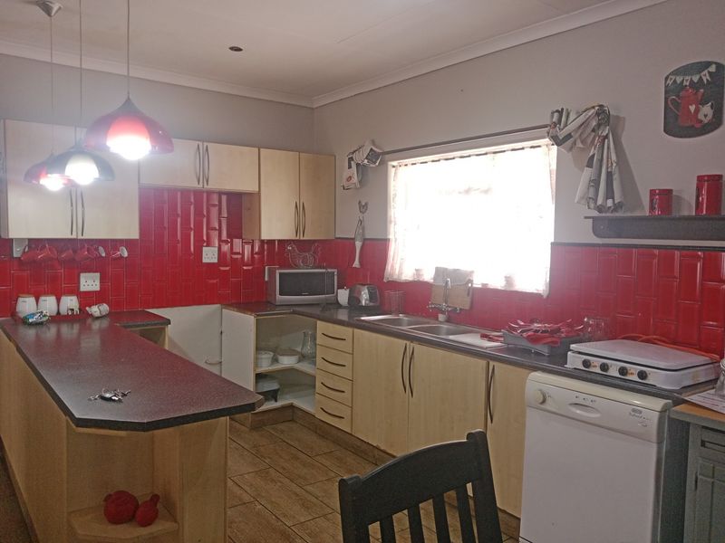 A functional kitchen featuring laminate cabinetry, a vibrant red subway tile backsplash, double bowl sink, and a breakfast bar with tiled flooring.