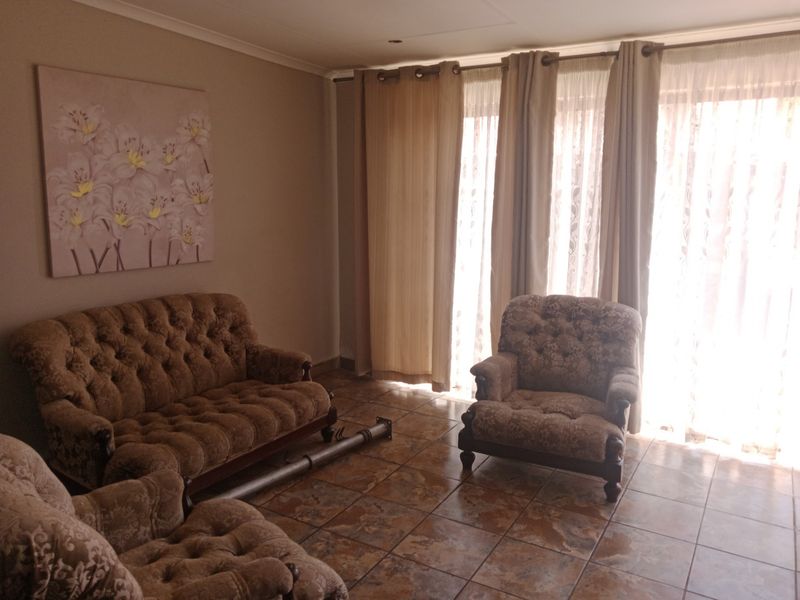 A living room featuring tiled flooring and large sliding glass doors with curtains, providing natural light and access to the exterior.