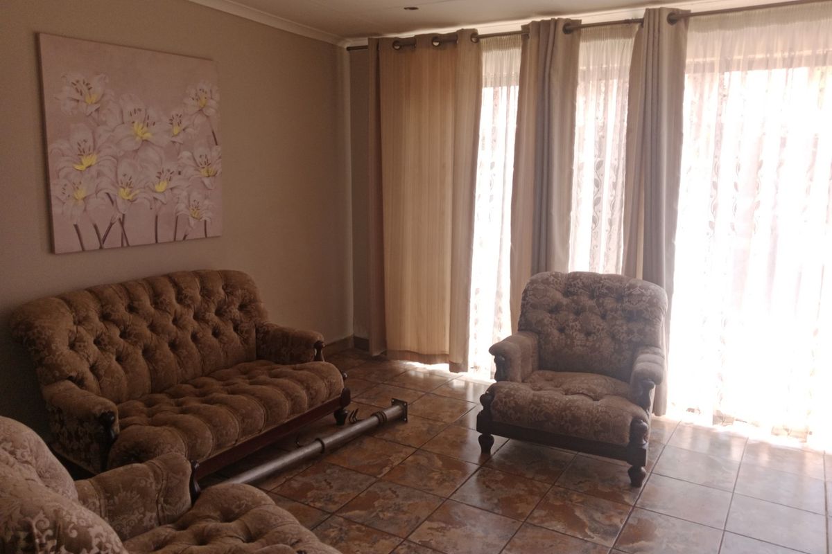 A living room featuring tiled flooring and large sliding glass doors with curtains, providing natural light and access to the exterior.