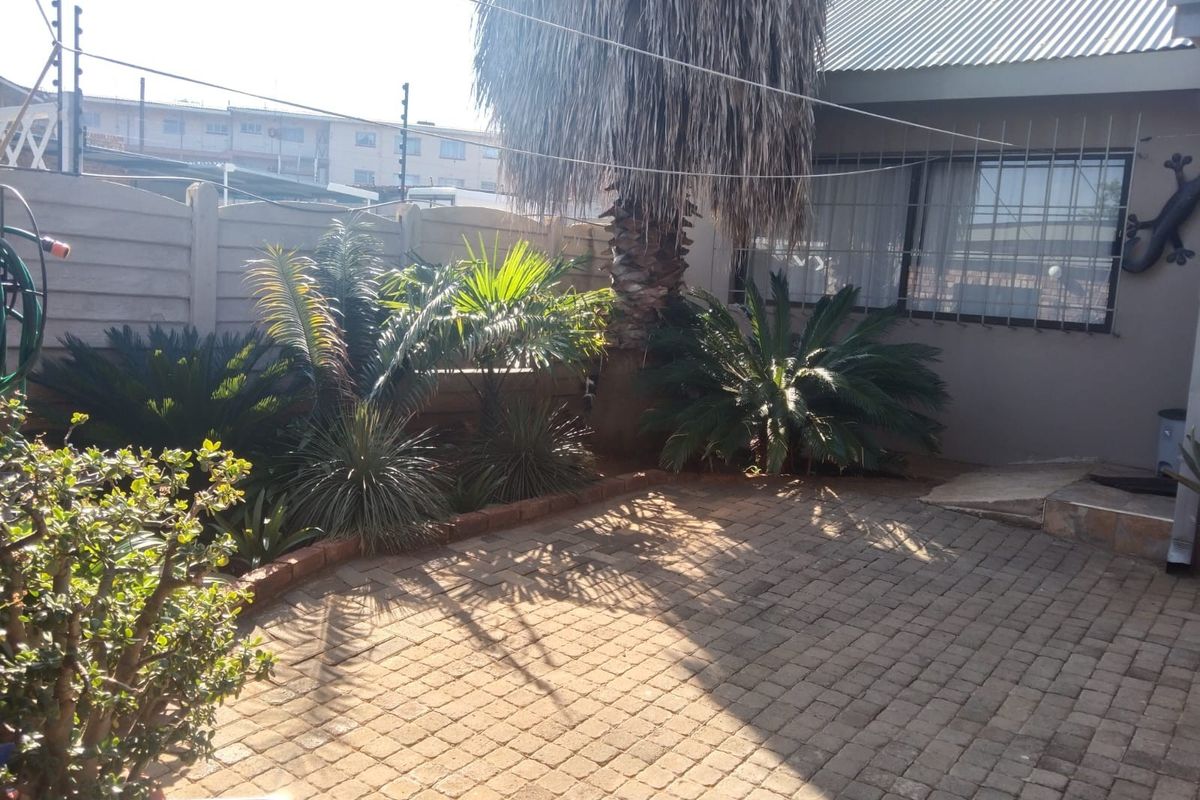 A rear courtyard area featuring paved flooring, a precast concrete boundary wall, and security bars on the windows.