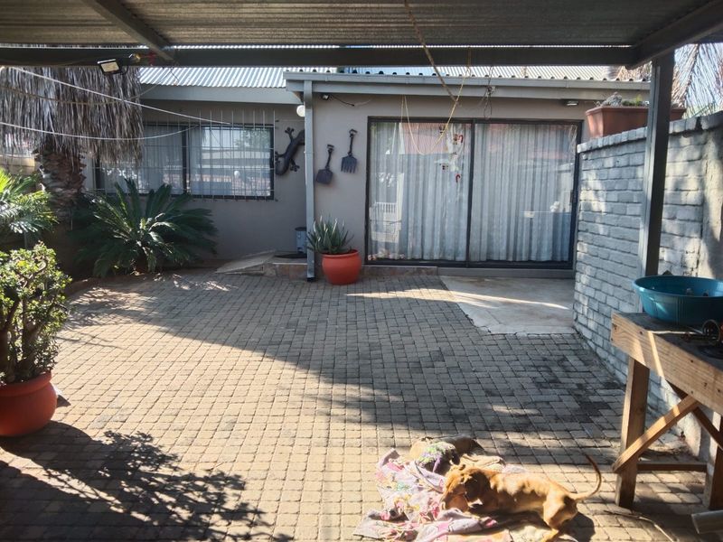 A covered outdoor patio area featuring brick paving, a sliding glass door entrance, and a corrugated metal roof structure.