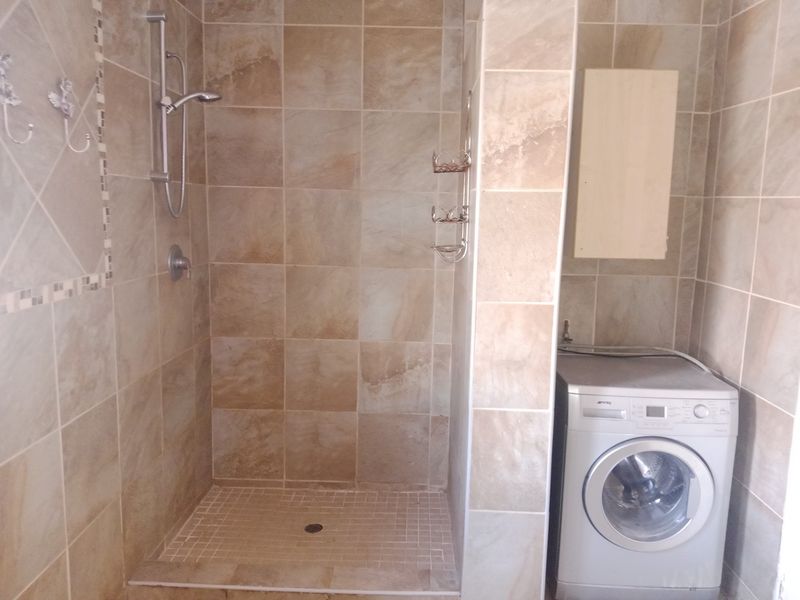 A functional bathroom featuring a tiled walk-in shower enclosure and a dedicated space for laundry appliances with built-in cabinetry.