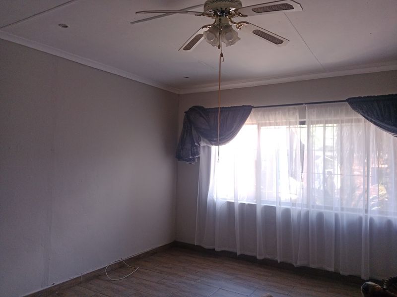 A vacant bedroom featuring tiled flooring, a ceiling fan, and window security bars, offering a neutral canvas for personalization.