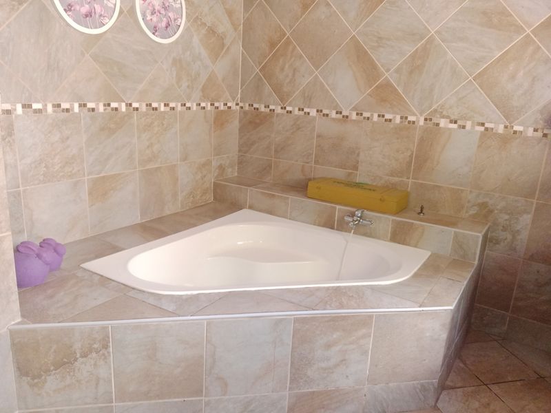 A corner bathtub featuring neutral-toned ceramic wall and deck tiling in a bathroom setting.