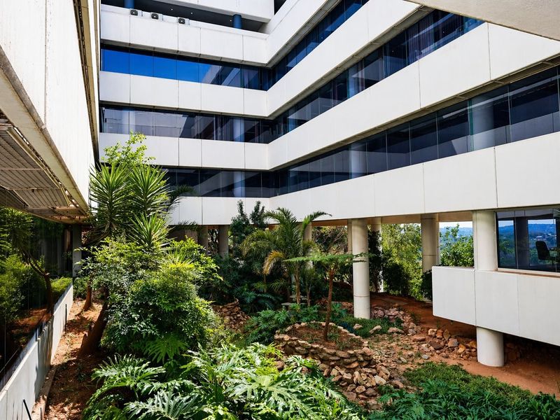 A view of a multi-story commercial building featuring a central landscaped courtyard with mature greenery and modern glass facade architecture.
