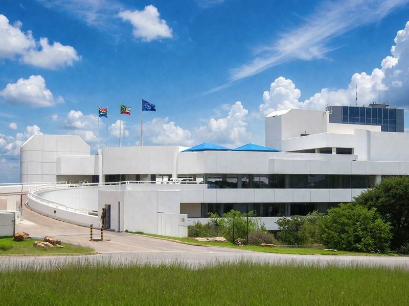 A modern commercial building featuring a prominent curved access ramp, multi-level white facade, and well-maintained surrounding grounds with flagpoles.