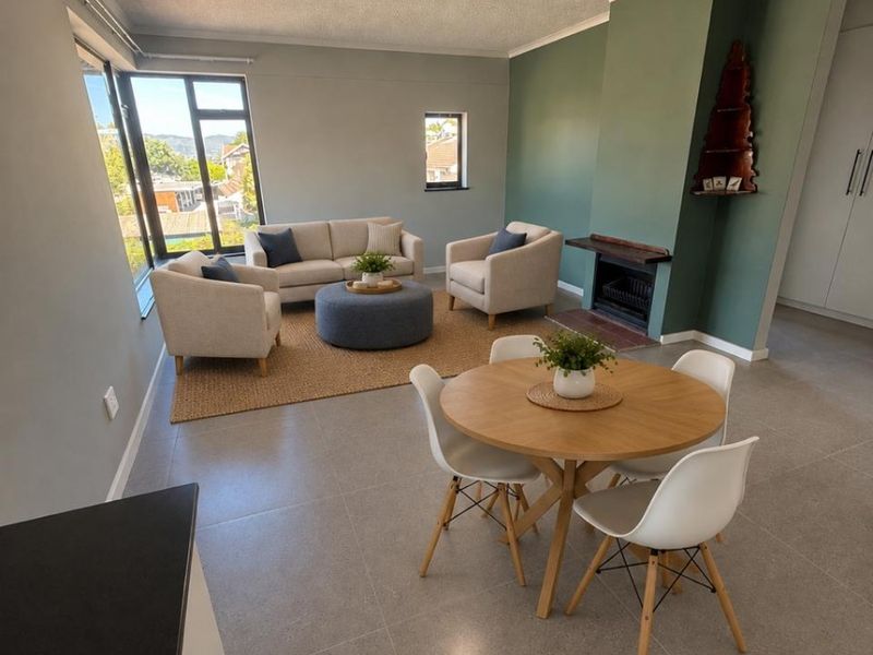 Spacious open-plan living and dining area featuring modern tiled flooring, a fireplace, and large windows providing natural light.