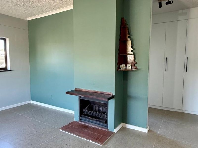 A bright, open living area featuring a central fireplace with a mantelpiece, neutral tiled flooring, and built-in storage cupboards.