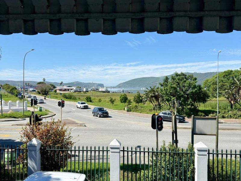 Elevated view overlooking a street intersection, surrounding landscape, and distant water, framed by a covered balcony structure.