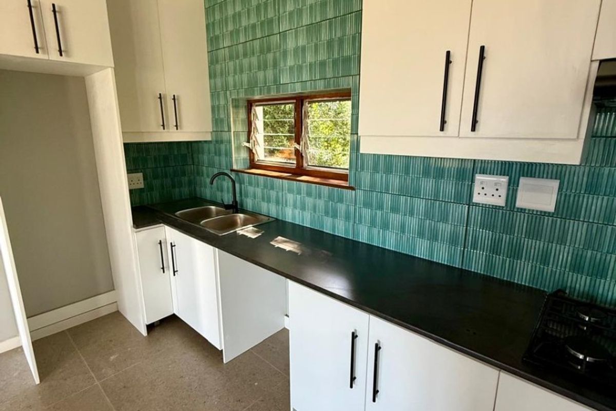 A bright, modern kitchen featuring white cabinetry, a striking green tiled backsplash, black countertops, and a built-in hob, offering a clean and functional space.