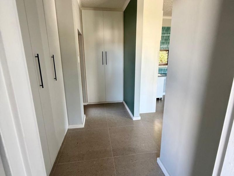 A clean, well-maintained hallway featuring neutral tiled flooring and ample built-in cupboard storage space.