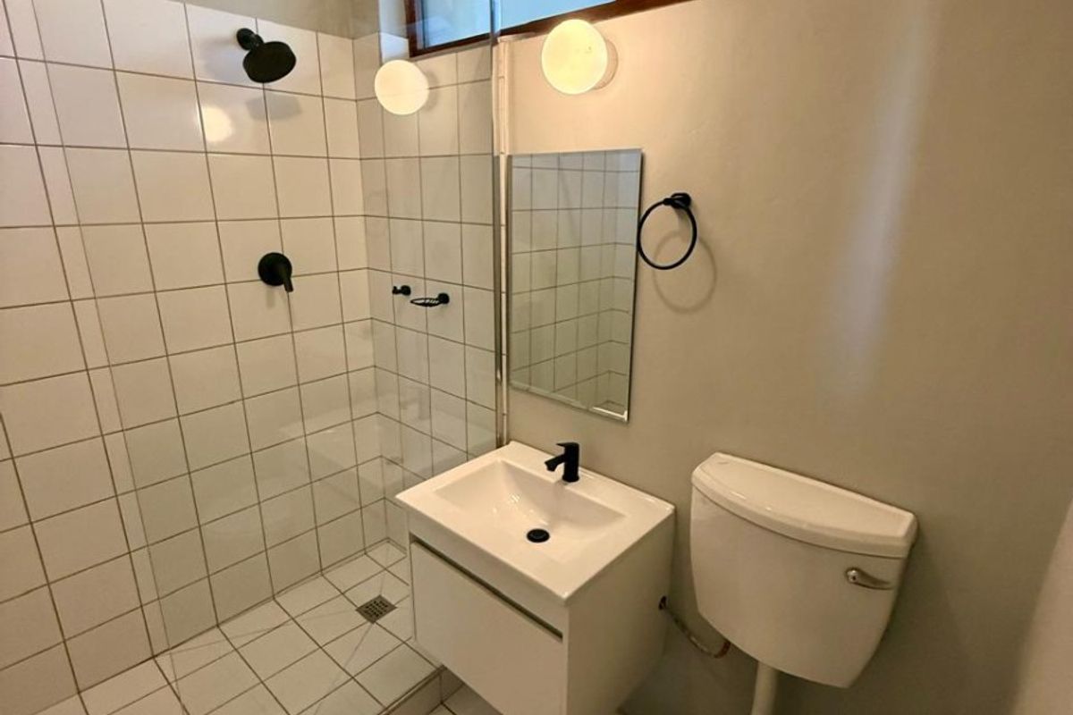 A modern, compact bathroom featuring a walk-in shower with glass screen, wall-mounted vanity, and louver windows for natural ventilation.