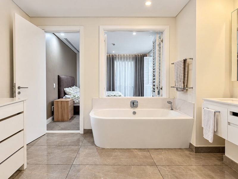 Modern bathroom featuring a sleek freestanding bathtub, vanity with basin, and an internal window providing a view into the adjacent bedroom.