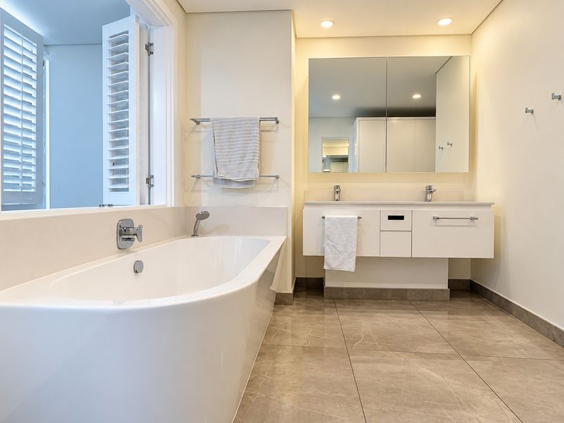 Modern bathroom featuring a sleek freestanding bathtub, double vanity with wall-mounted cabinetry, and high-quality tiled flooring in a bright, well-lit space.