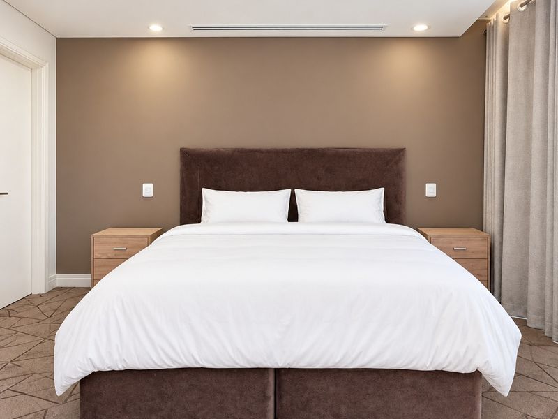 A well-maintained bedroom featuring neutral wall tones, recessed downlighting, ducted air conditioning, and patterned carpet flooring.