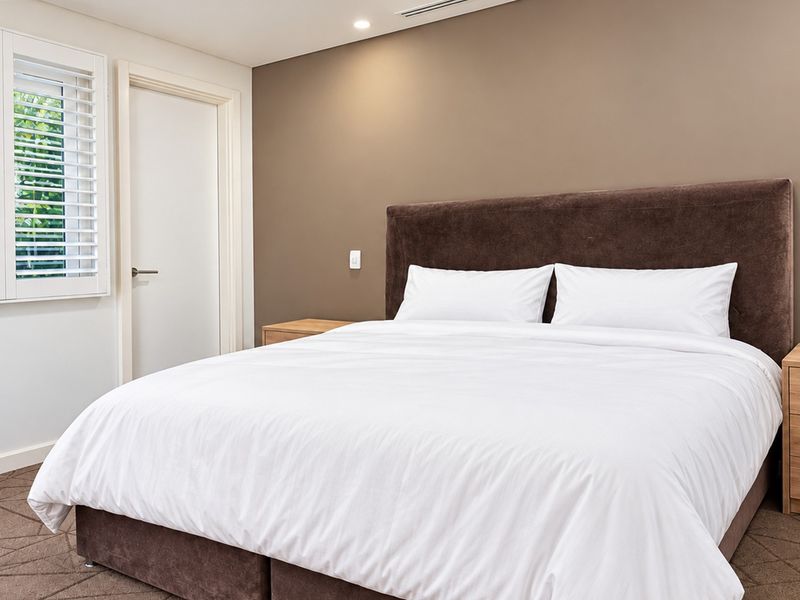 A well-maintained bedroom featuring neutral wall tones, plantation shutters, recessed lighting, and ducted air conditioning.