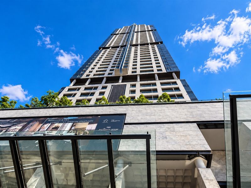 Low angle view of a modern high-rise apartment building featuring stone cladding, glass facade, and a contemporary glass entrance canopy.