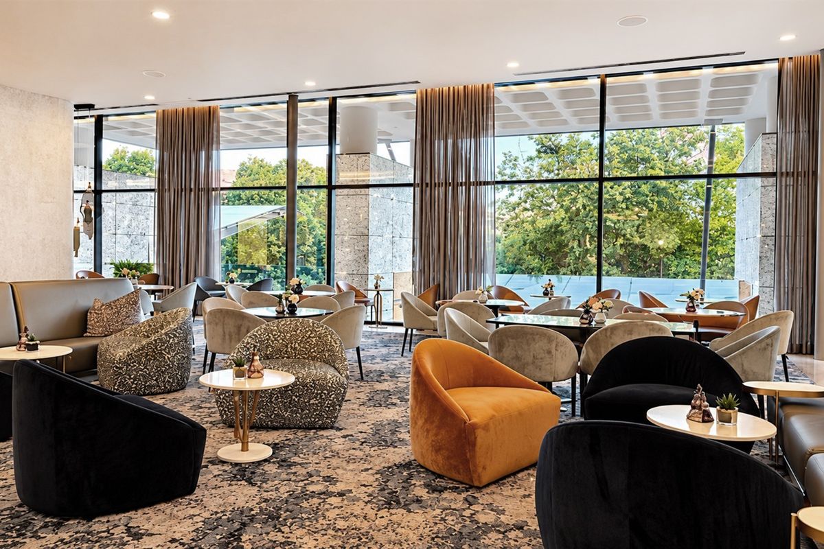 A spacious, modern lounge area featuring floor-to-ceiling windows that provide ample natural light and views of the surrounding greenery.