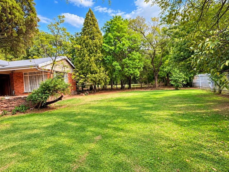 A spacious, well-maintained garden featuring a lush lawn, mature trees, and a brick-faced home exterior with a stone retaining wall.
