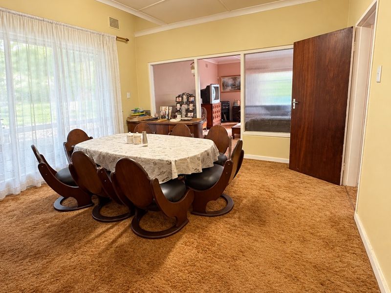 A dining room featuring dated carpet flooring, a textured ceiling, and a fluted glass partition wall leading to an adjacent living space.