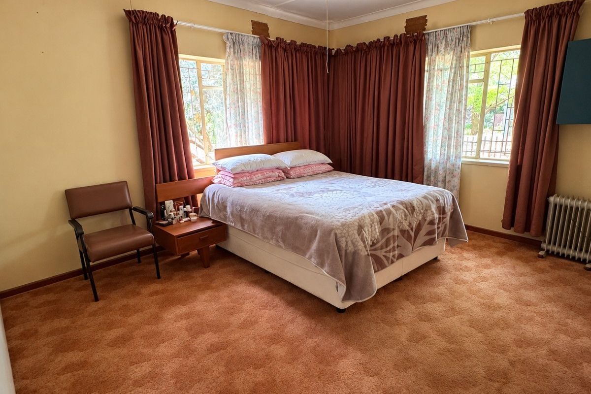 A spacious bedroom featuring a ceiling fan, radiator heating, and carpeted flooring, offering a blank canvas for modernization and interior updates.