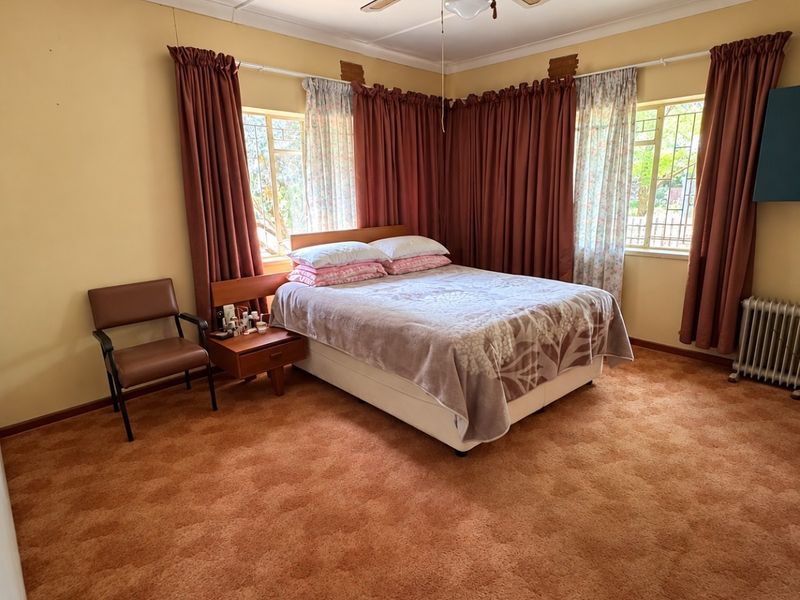 A spacious bedroom featuring a ceiling fan, radiator heating, and carpeted flooring, offering a blank canvas for modernization and interior updates.