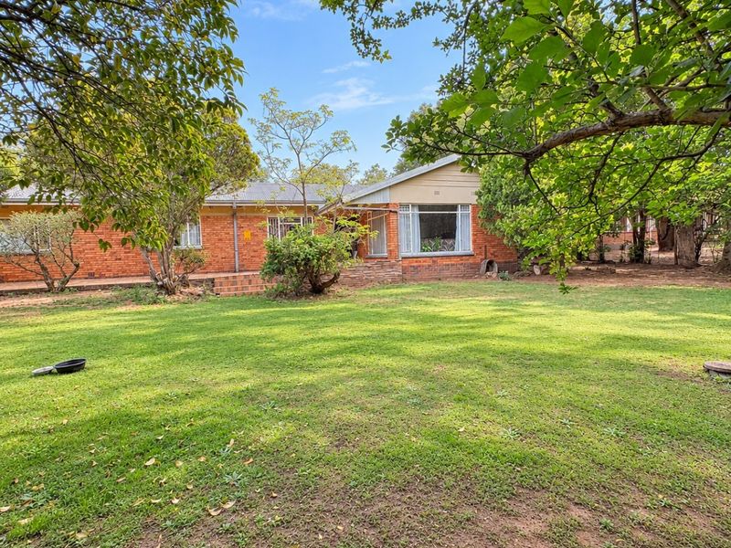 A view of the rear brick facade of the house, featuring a large established garden and a paved patio area.