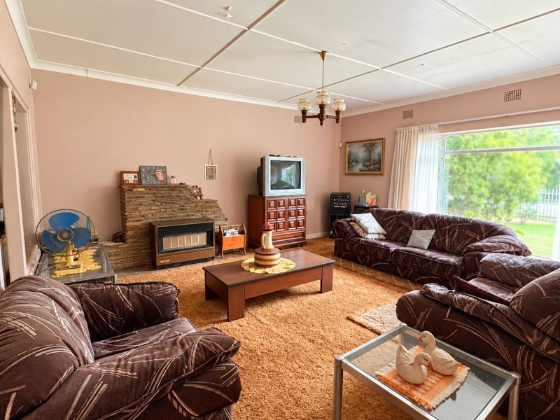 Spacious living room featuring a stone fireplace with a built-in gas heater, large window for natural light, and traditional ceiling tiles.