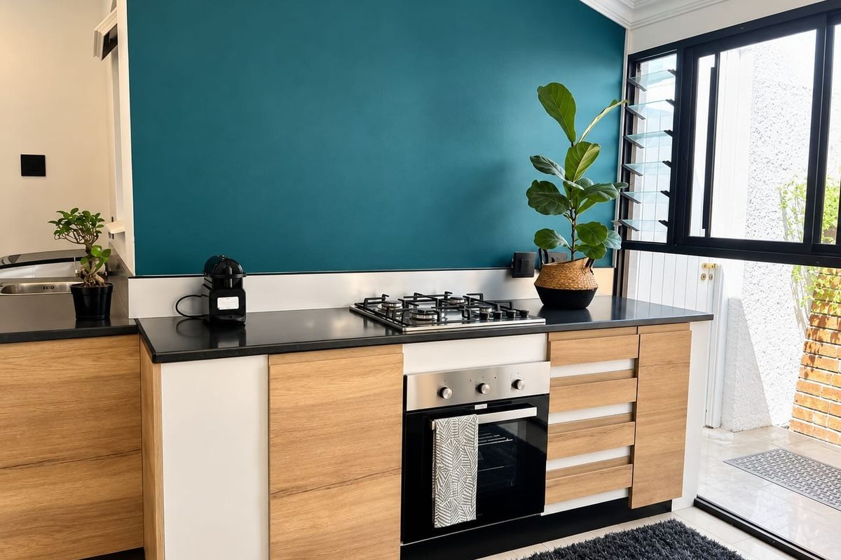 Modern kitchen featuring wood-tone cabinetry, black stone countertops, a gas hob, and a built-in oven, set against a bold teal accent wall.