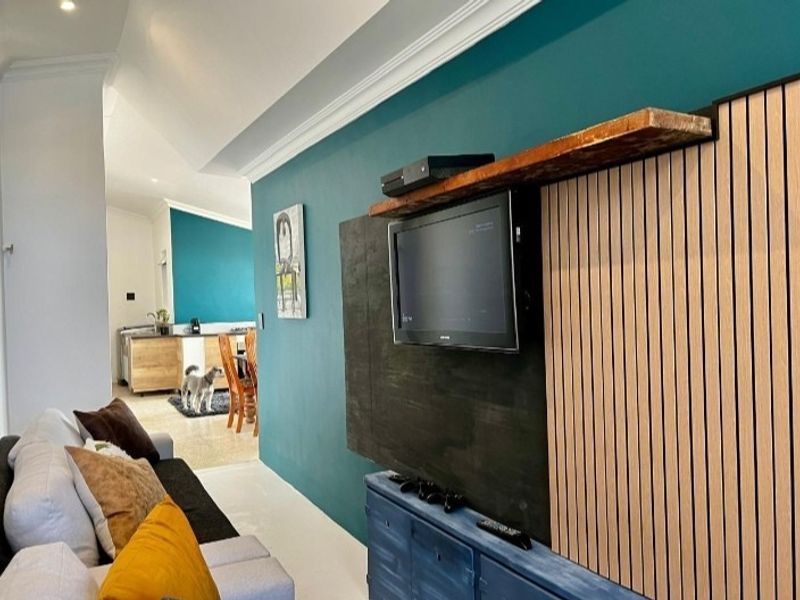 A modern living room featuring a decorative slatted timber feature wall with a floating shelf and recessed ceiling lighting.